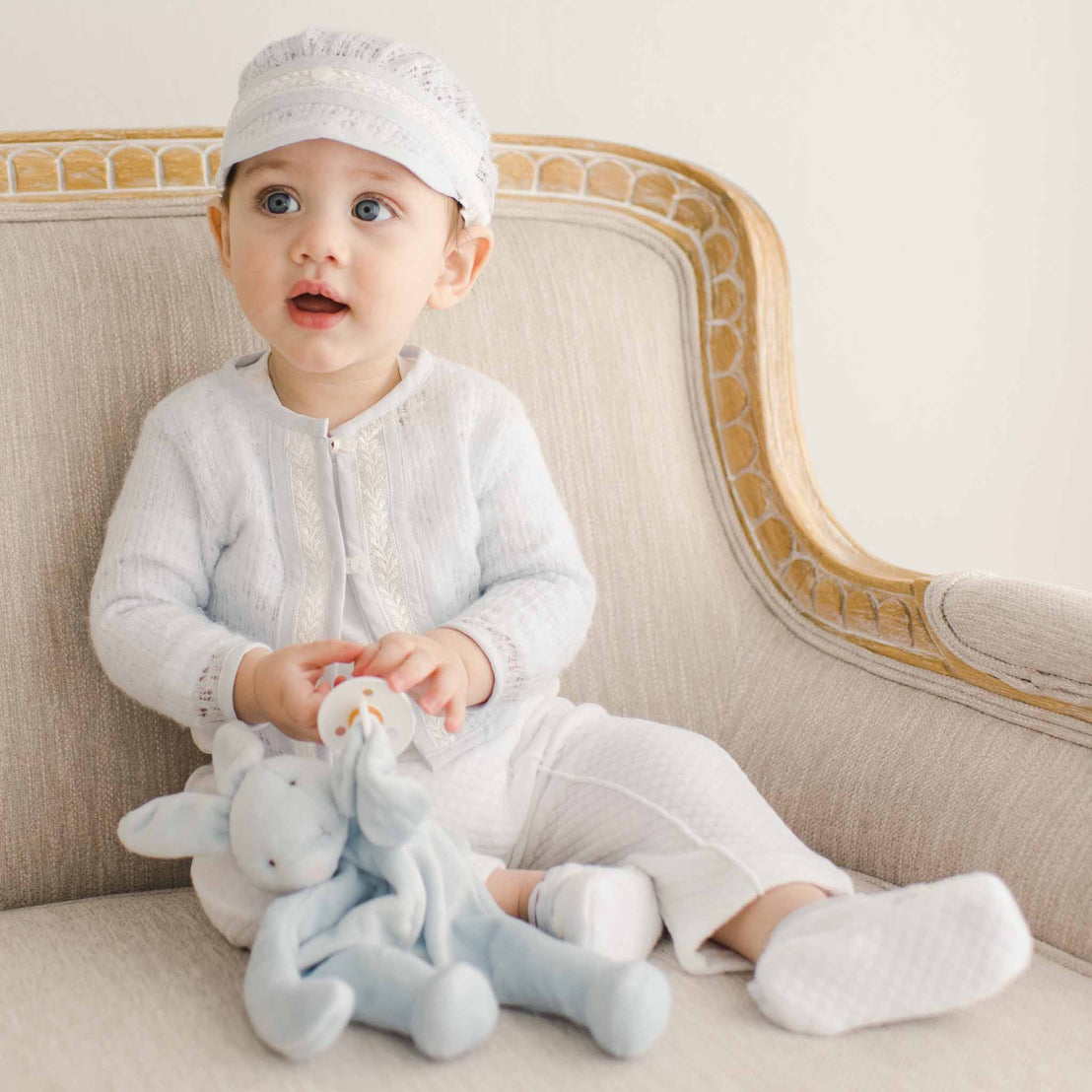 Baby boy sitting on a chair and wearing a Harrison 3-piece pant suit and matching blue knit sweater. He is holding a blue bunny stuffed animal