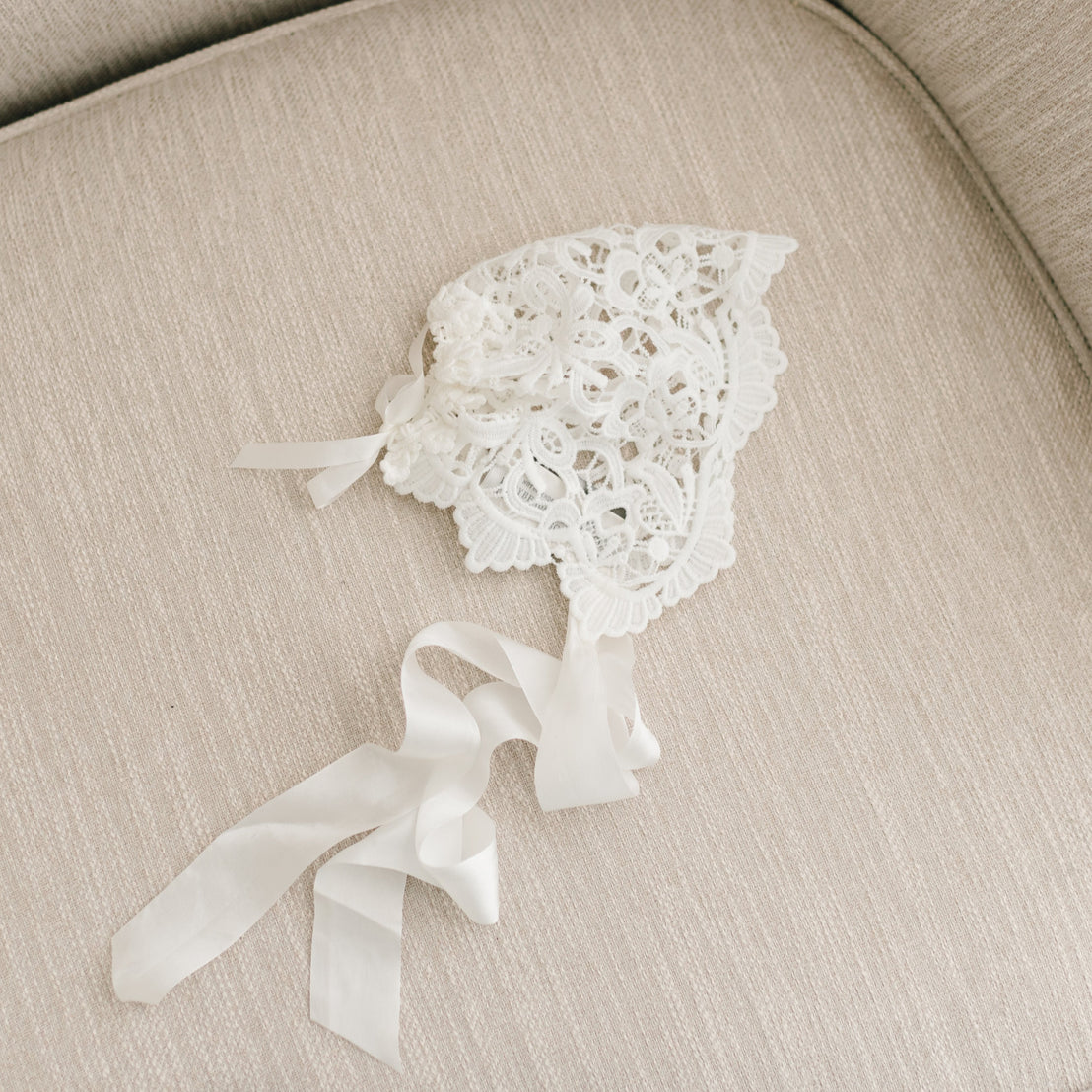 Flat lay of the Lola Lace Bonnet, featuring richly embroidered ivory lace with a floral lace edge at the back.