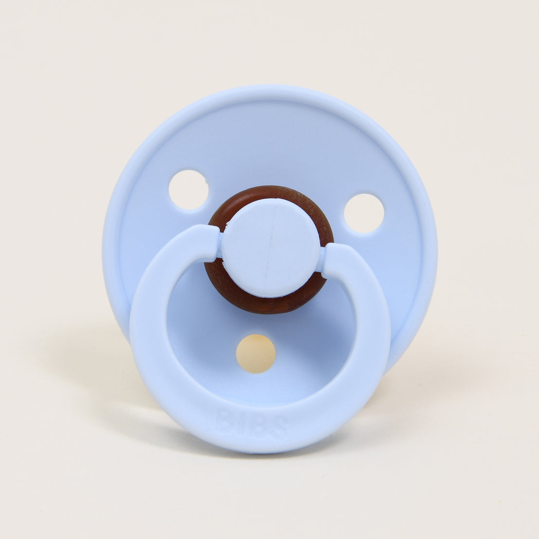 A Bibs baby pacifier in "baby blue" color with three ventilation holes and a brown ring handle set against a plain light background.