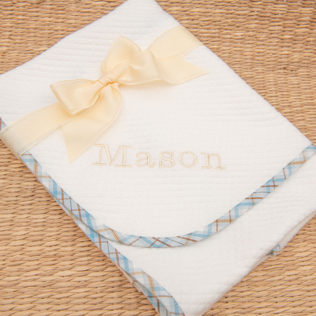 A Mason Personalized Blanket with the name "Mason" embroidered in gold thread, blue plaid trim on an upscale textured woven background, perfect for baptism. The blanket is presented with a featuring a vintage yellow/gold satin bow.