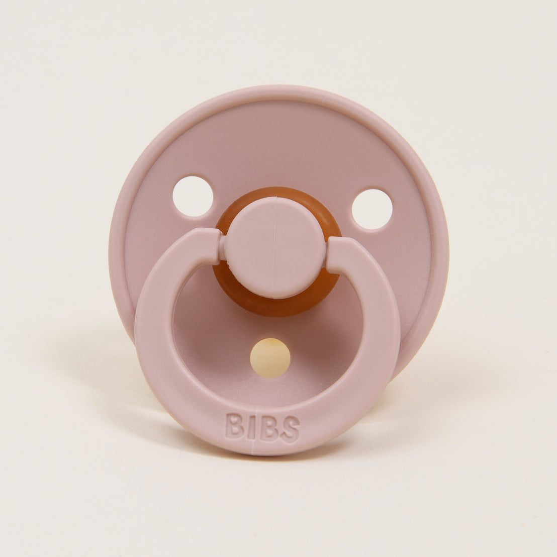 A Bibs Pacifier Set in Blush with two ventilation holes, featuring a brown pull ring and a yellow tip on a neutral background.