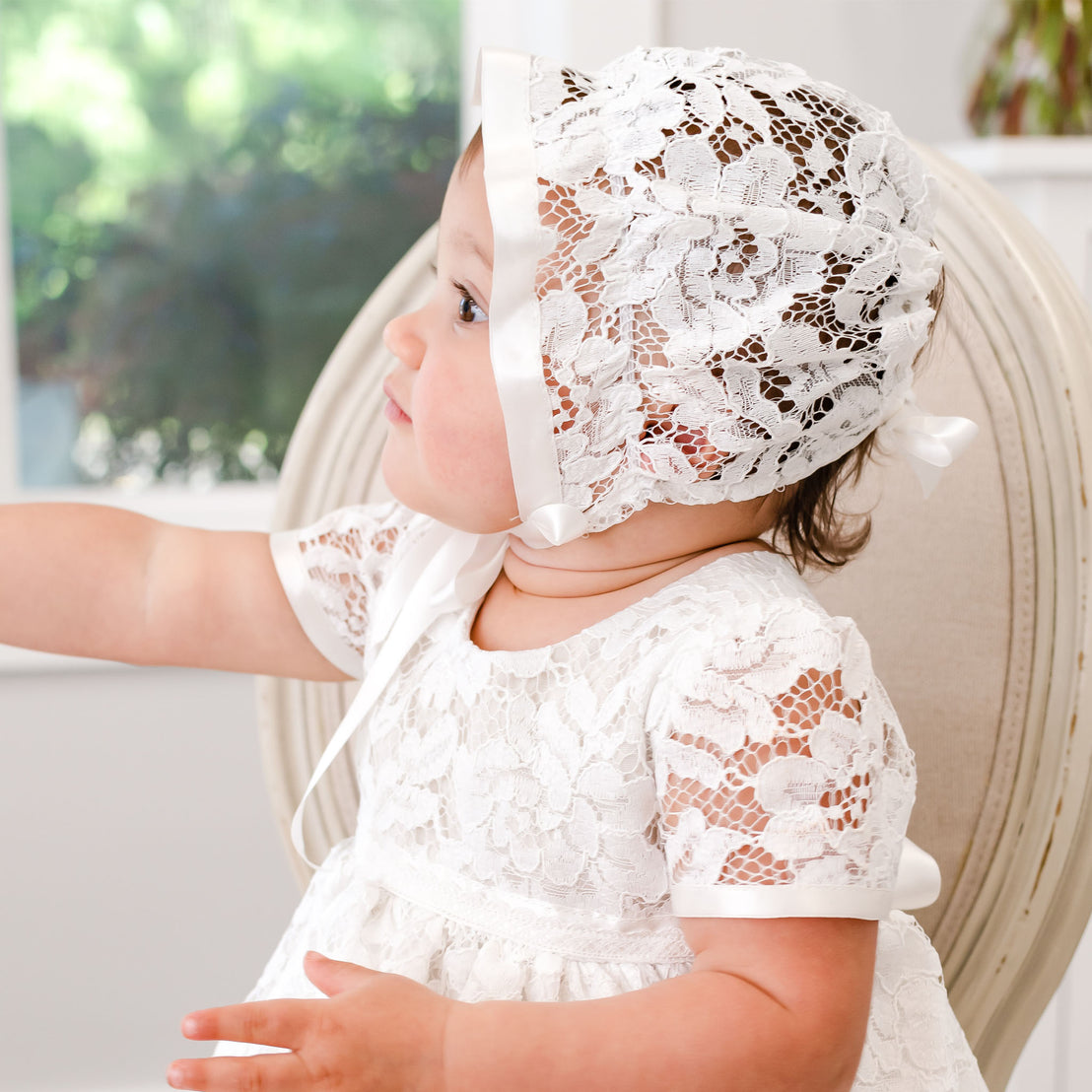 A baby in a Rose Christening Gown & Bonnet for baptism.