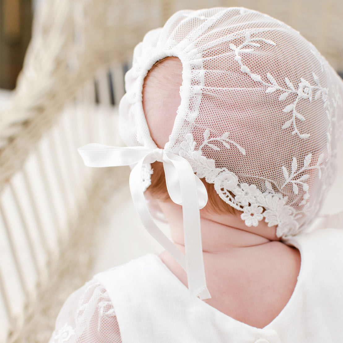 A close-up image of a baby wearing an Isla Lace Bonnet, showcasing the back  of the bonnet. The lace bonnet features intricate floral embroidery and silk ribbon ties.