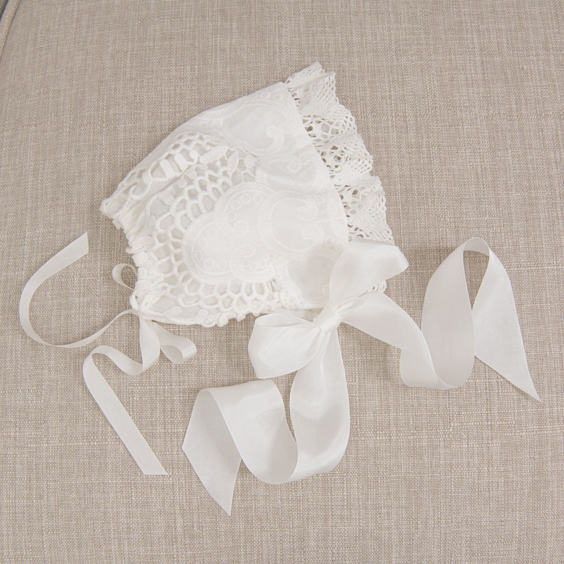 Flat lay of the Lily Bonnet made with light ivory cotton lace, light ivory edge lace, and ivory silk ribbon