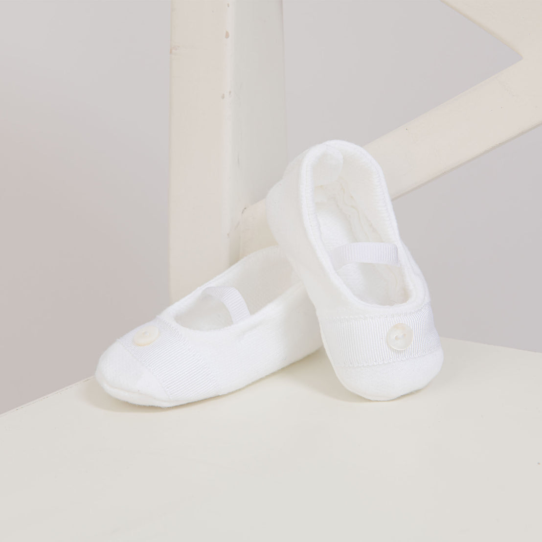 Flat lay photo of a pair of Elliott Booties made from white French terry and featuring grosgrain ribbon detailing across the toe with a button.