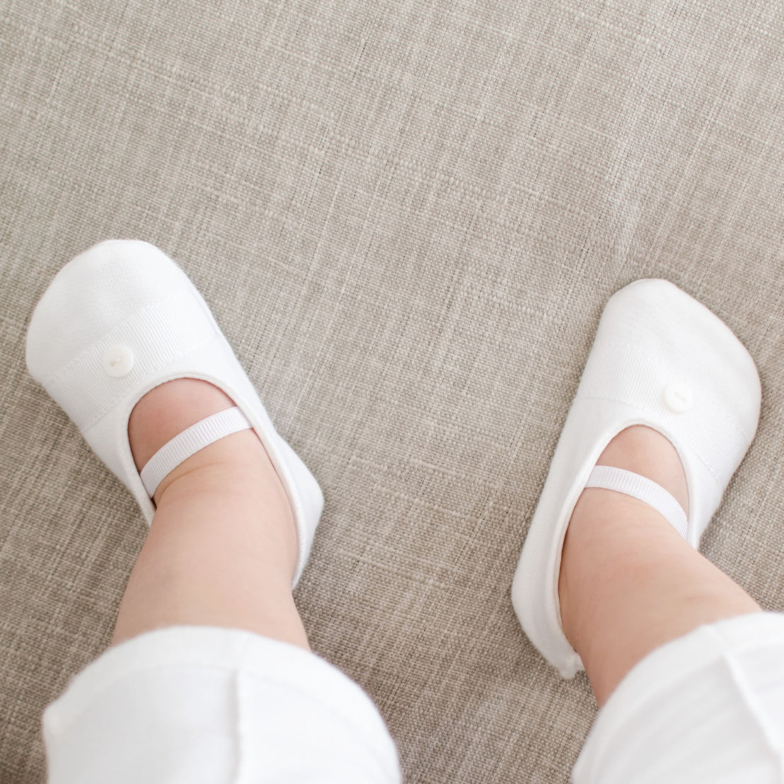 Baby boy wearing the White French Terry Booties. Made from 100% French Terry Cotton and features a grosgrain ribbon detail across the toe with a button.