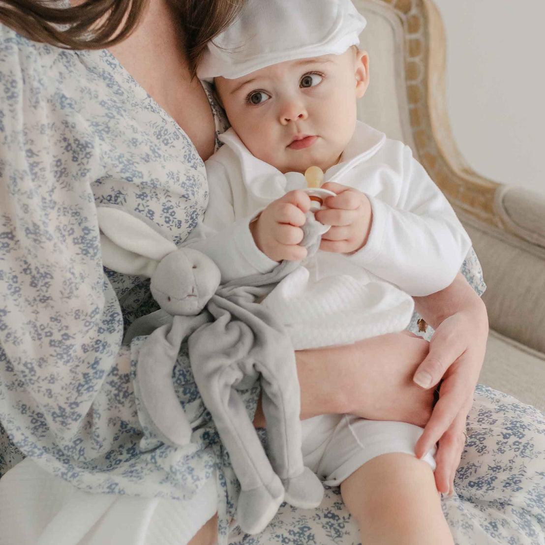 Baby boy with his mother. He is holding onto the Miles Silly Bunny Pacifier Holder, a grey bunny stuffed animal