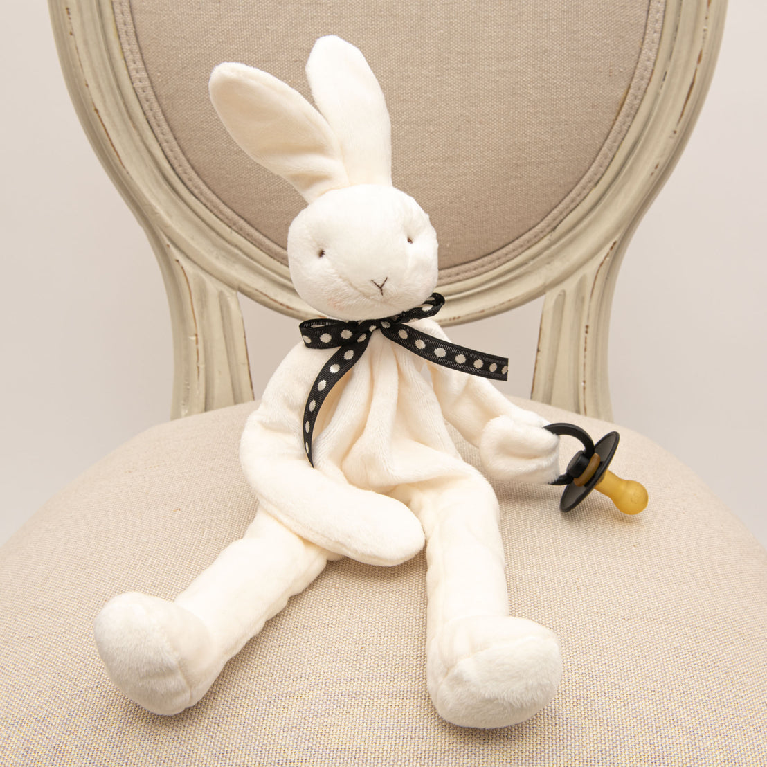 Flat lay of the James Silly Bunny Buddy, a white floppy stuffed animal bunny made from soft velour and can hold on to a pacifier. 