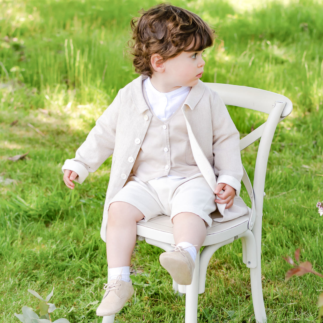 Baby boy sitting on a chair outside and wearing the tan Silas Trench Coat