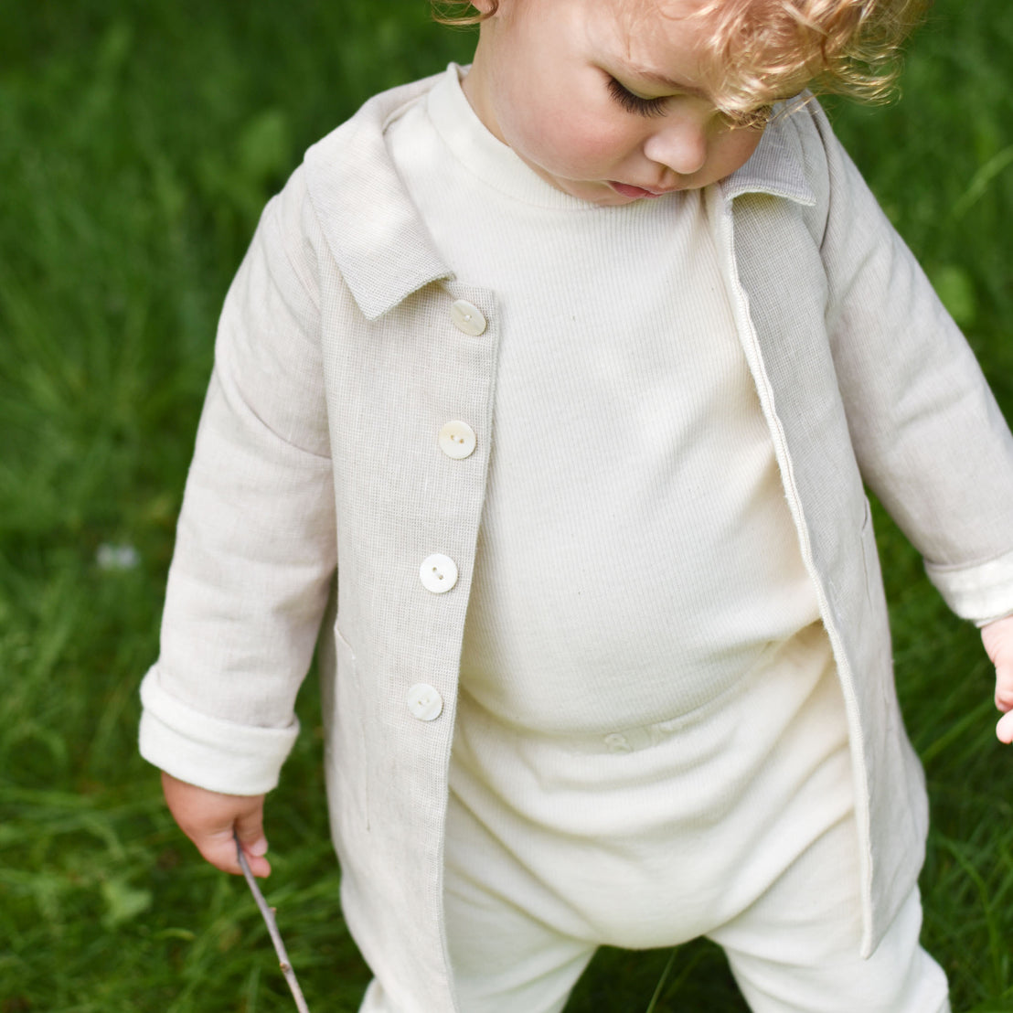 Baby boy out in the forest wearing the tan Silas Trench Coat layered over a cotton ribbed shirt