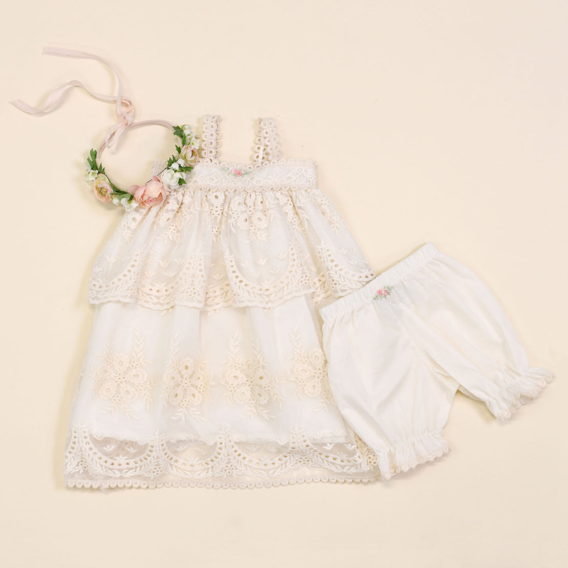 A delicate Clementine Dress & Bloomers set for a toddler, displayed flatly on a light beige background, complemented by a floral headband.