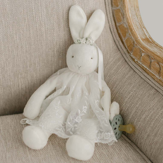 A flat lay photo of the Ella Silly Bunny Buddy dressed in a mini Ella Lace Romper Dress and floral headband.