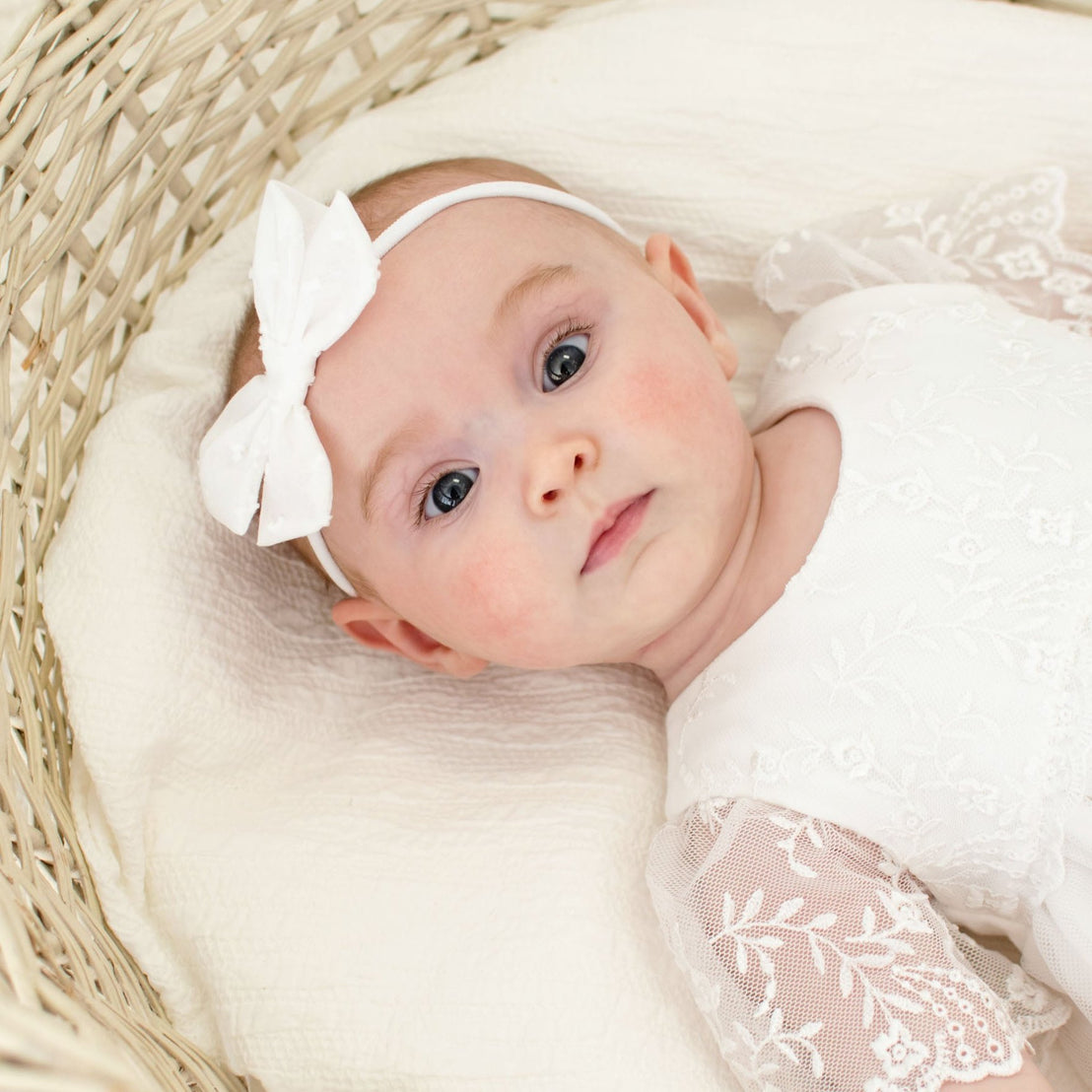 A newborn baby girl gazes into the camera with wide eyes, wearing the Ella Baby Girl Headband and matching romper dress.