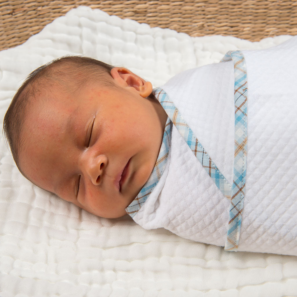 A newborn baby sleeps peacefully, swaddled in a Mason Personalized Blanket with a blue and brown diamond pattern.