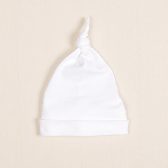 The Newborn Knotted Cap, also known as the Liam Cap, is displayed flat on a beige background, making it an ideal choice for a soft and stylish newborn outfit.