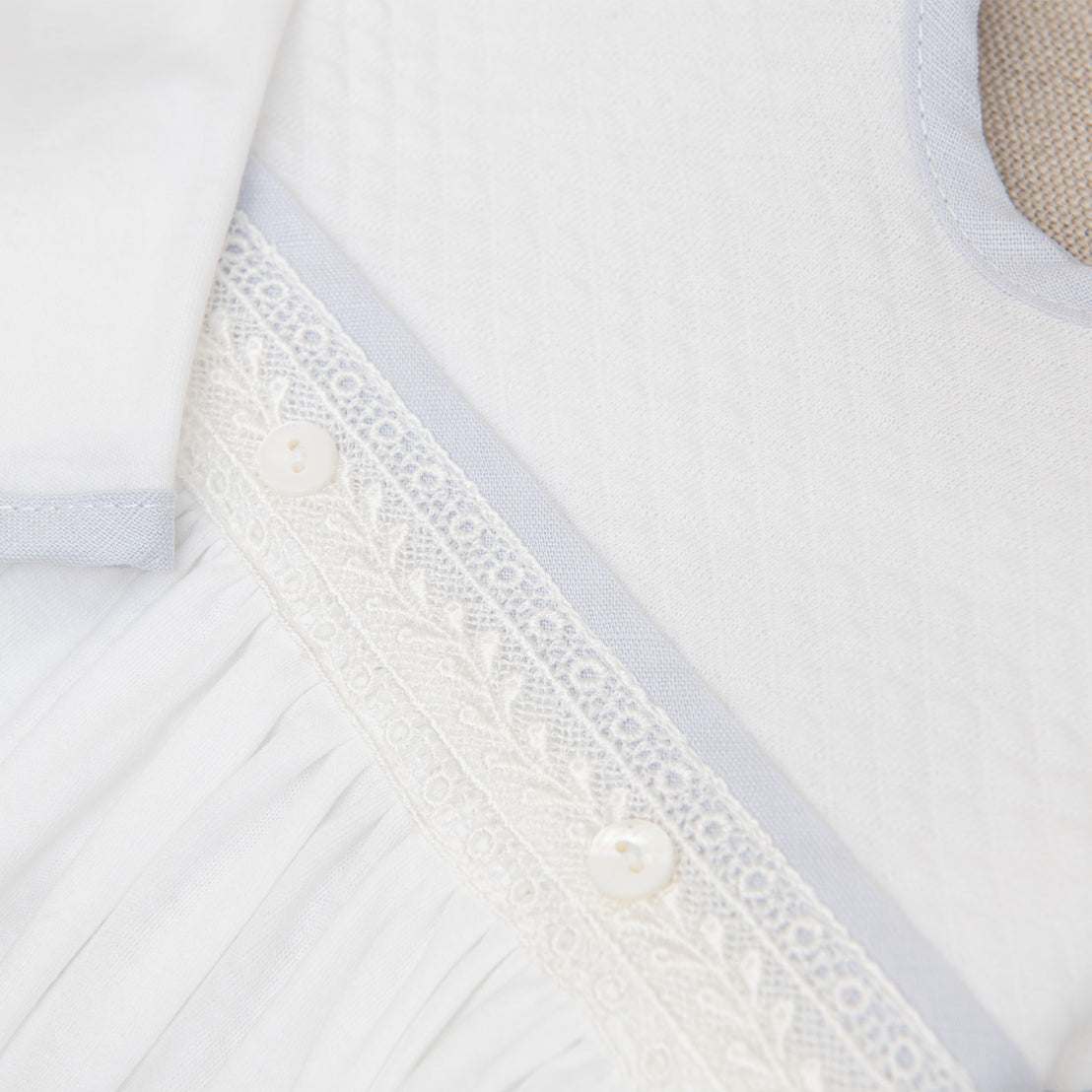 Close up detail of the Harrison Newborn Gown featuring the ivory Venice lace accent along the bodice and light blue linen trim