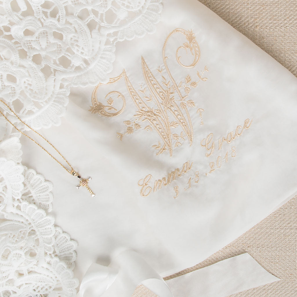 Close-up of the monogram on the Lola gown, featuring a detailed embroidered 'W' initial, with the name 'Emma Grace' and the date '3-13-2018,' showcasing personalization options for christening or birth.