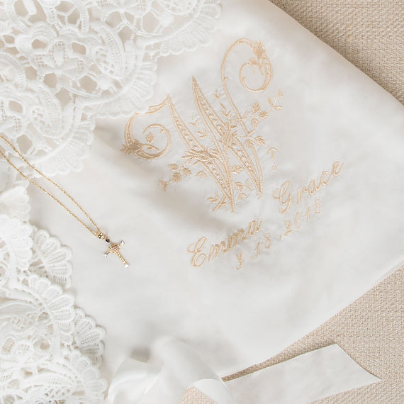 Close-up of the monogram on the Lola gown, featuring a detailed embroidered 'W' initial, with the name 'Emma Grace' and the date '3-13-2018,' showcasing personalization options for christening or birth.