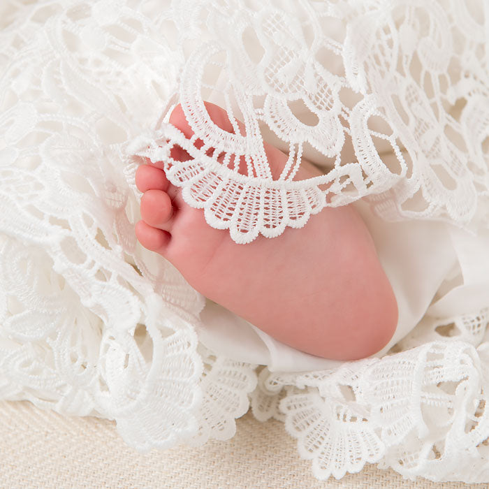 Photo showcasing the linen lace overlay that is a part of the Lola Dress. A baby foot appears among the linen lace.