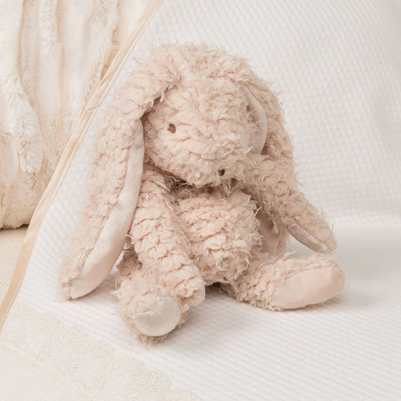 A vintage Harey Bunny toy with fluffy, textured fur and floppy ears, sitting on a striped, white fabric, with a soft beige heirloom blanket partially visible in the background.