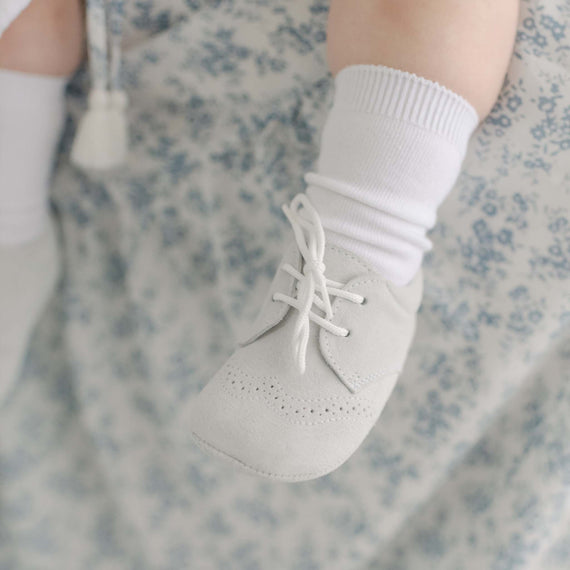 Photo of a baby foot wearing the Miles Suede Shoes. Made with a soft grey suede with detailed edging. 