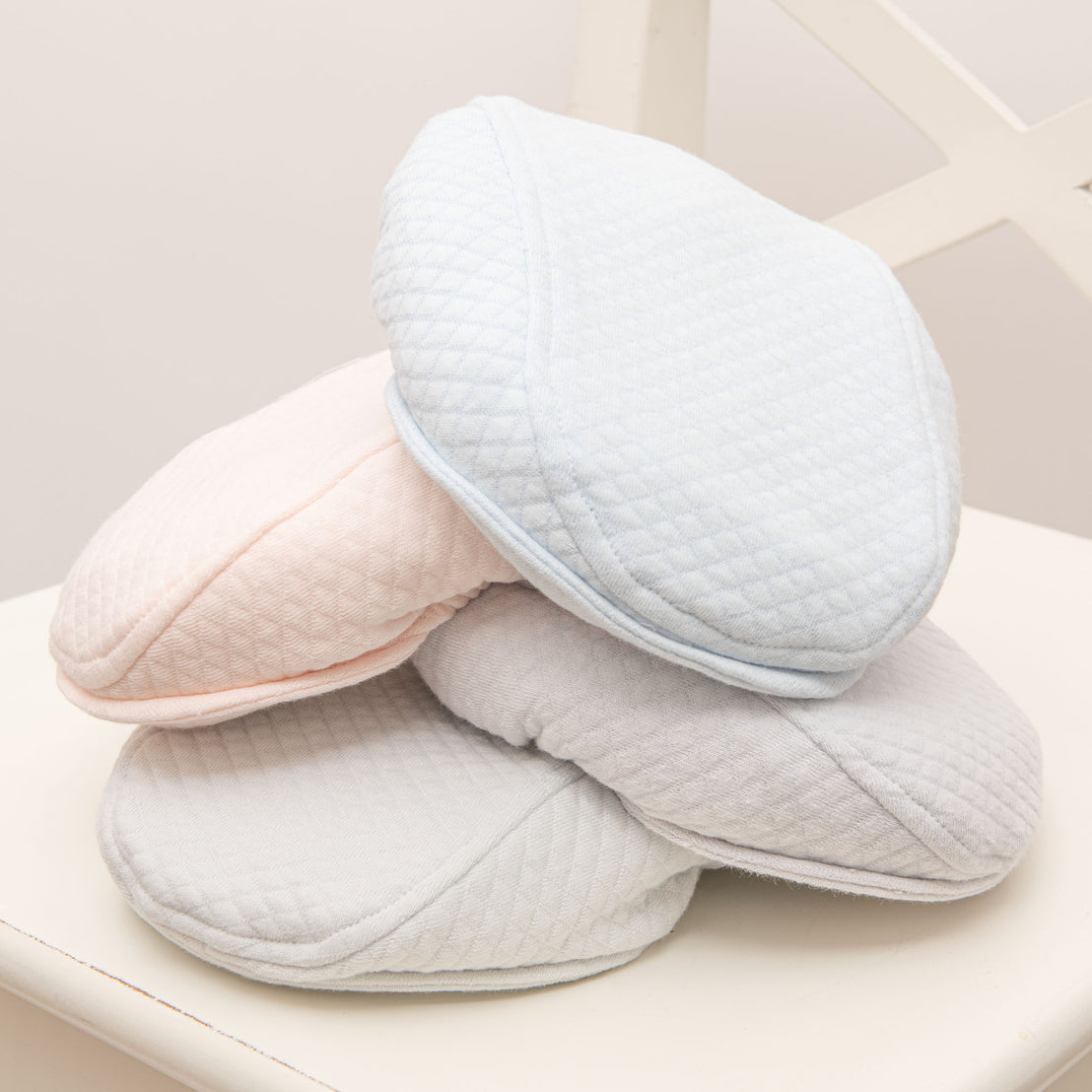 Flat lay photo of the four Asher Quilted Newsboy Caps in colors grey, pink, powder blue and soft teal.