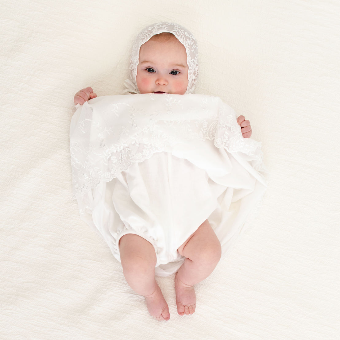 A baby girl holding up her skirt showcasing the undergarment of the Ella baptism dress.