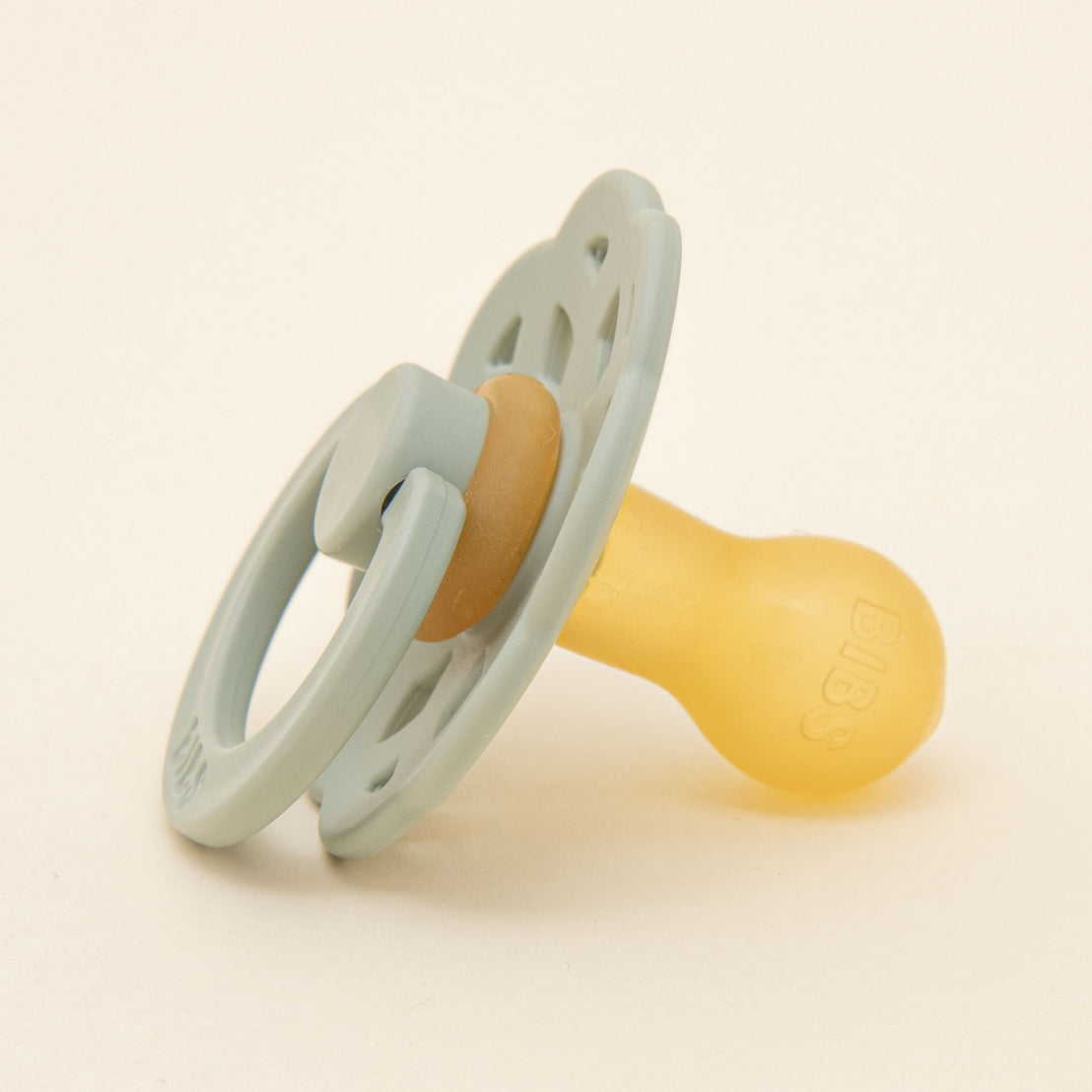 A sage green Bibs Lace Pacifier set against a light beige background. The pacifier, designed in Denmark, features a rounded natural rubber nipple and a ventilated, ergonomic shield.