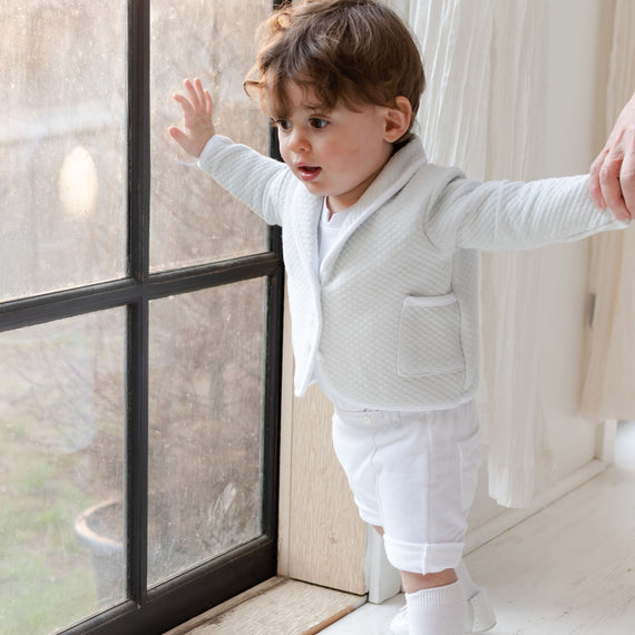 Baby boy by window wearing a teal baby boy suit with a pair of shorts.