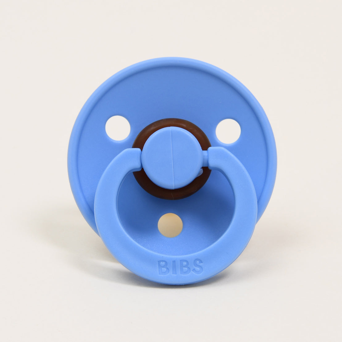 A  bibs pacifier in "sky blue" with a natural brown ring and the brand name "bibs" embossed on the front, set against a plain off-white background, perfect as an upscale baby gift.