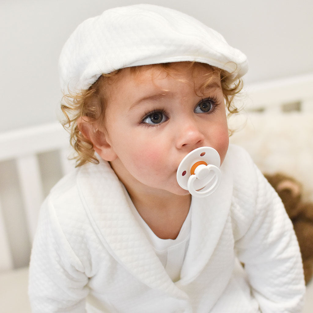 Photo of a baby boy wearing the Elijah Newsboy Cap with a white pacifier in his mouth 