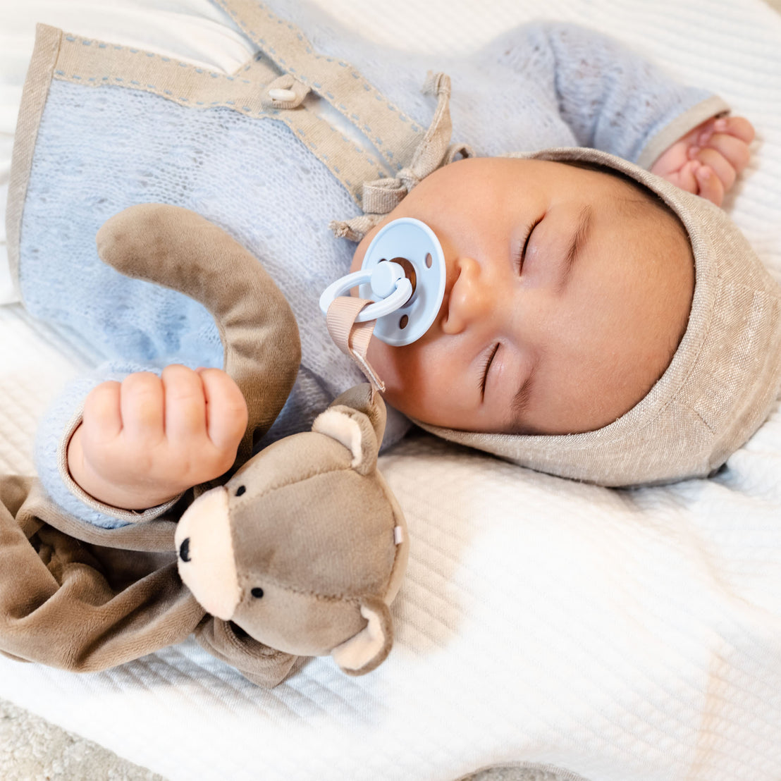 Baby sleeping in the Baby Beau & Belle Austin outfit, soft sweater and linen bonnet. A soft plush teddy bear sits by his side.