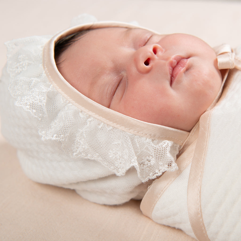 Newborn baby girl wearing the Tessa Quilt Bonnet made from a quilted cotton in white and trimmed in pink champagne silk and light ivory floral lace.