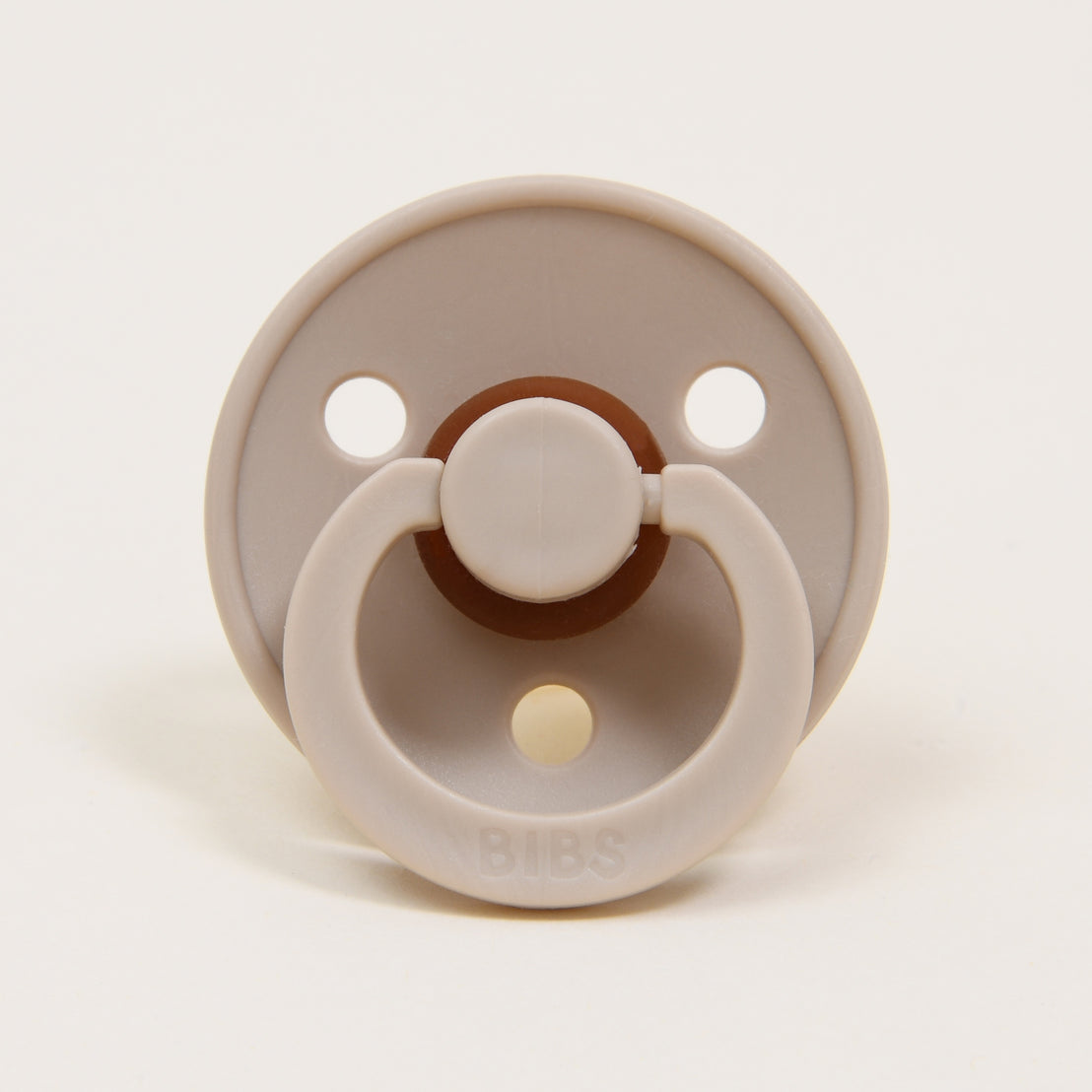 A Braden Pacifier Set | Vanilla & Ivory with two large holes, a brown button-style handle, and the brand name "bibs" in the center, isolated against a white background, making it an ideal upscale baby gift