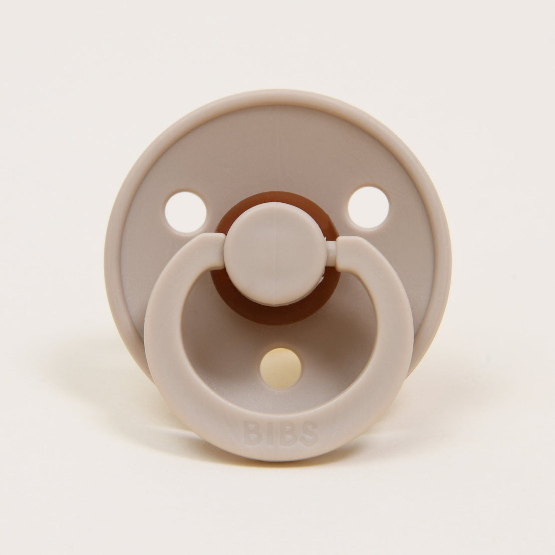 A bibs pacifier in the color vanilla, photographed against a beige backdrop.