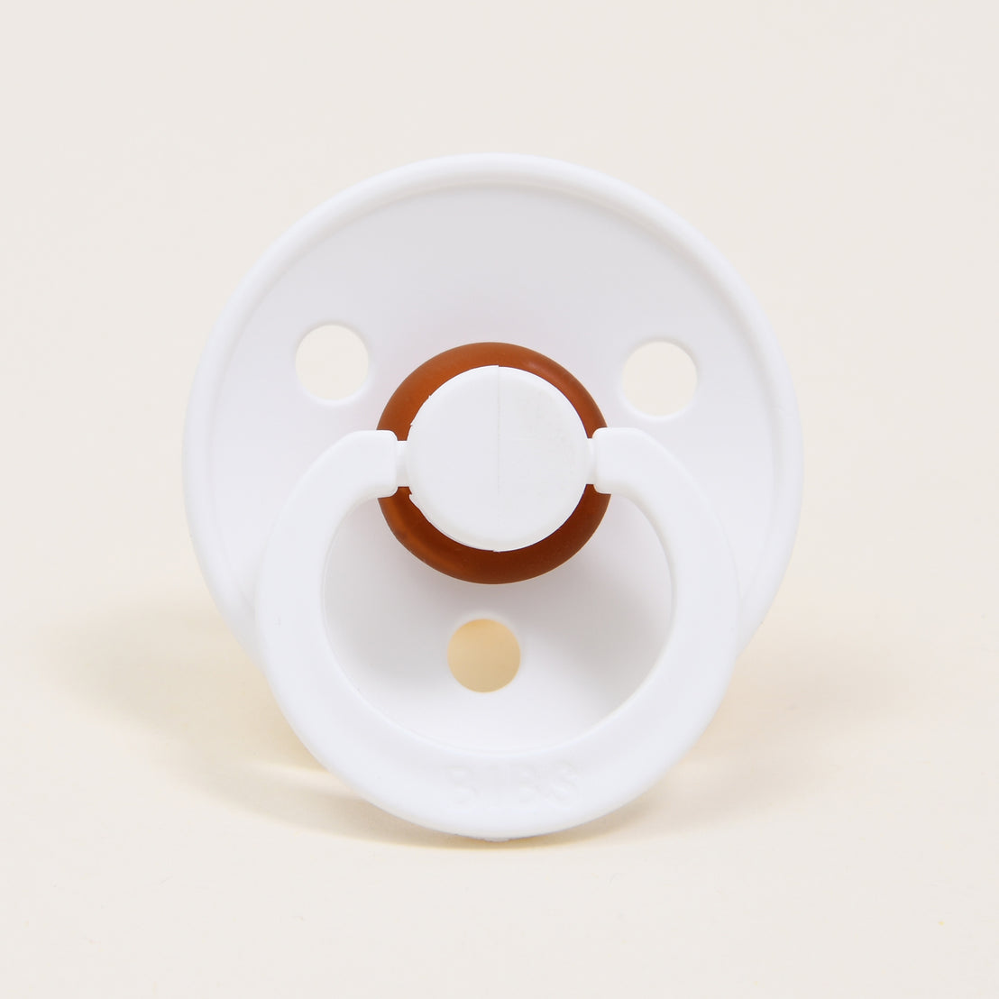 A white bibs pacifier set against a beige background. 