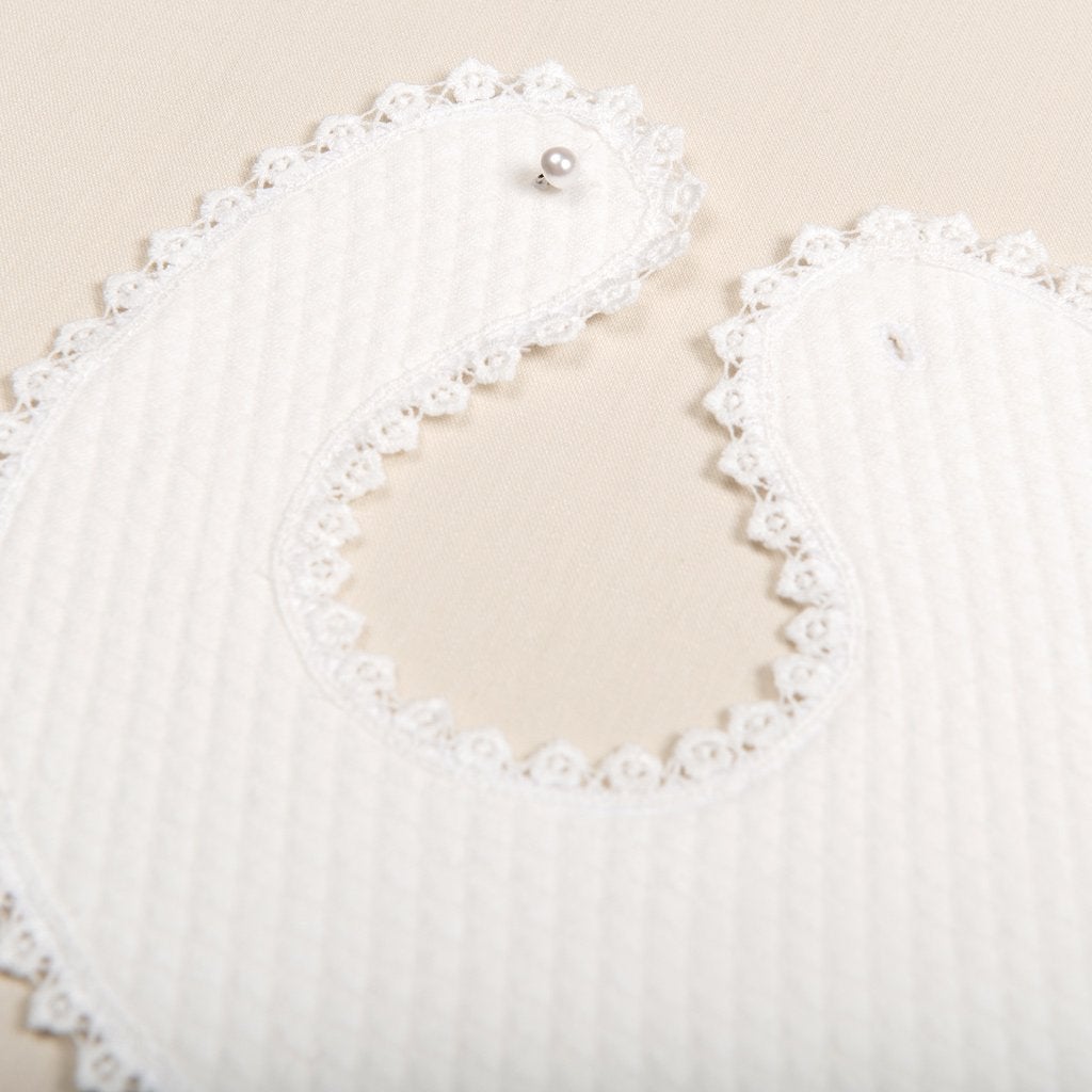 Close up details of a christening bib on a beige flat surface.